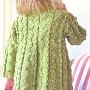 Könnte beinhalten: Eine hellgrüne Strickjacke mit einem strukturierten Zickzackmuster. Der langärmlige Pullover hat einen runden Ausschnitt und ist aus einem weichen, möglicherweise wollenen Material gefertigt. Die Rückseite der Strickjacke ist sichtbar und zeigt das komplizierte Stichdesign.