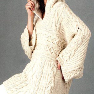Può includere: Un maglione di lana color crema con un ampio cappuccio e dettagli a treccia. Il maglione ha una vestibilità rilassata e una silhouette lunga e fluida.