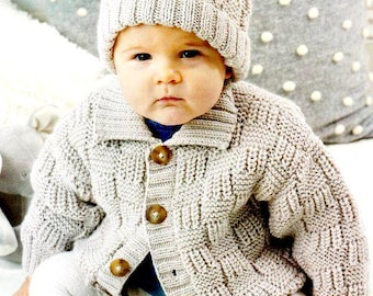 May include: A baby wearing a light gray knitted hat with a pom-pom and a matching cardigan. The cardigan has a collar and three brown buttons. The baby is also wearing white leggings.