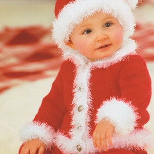 May include: A baby wearing a red knitted Santa suit with white fur trim. The suit has a button closure and the hat has a white pom-pom.