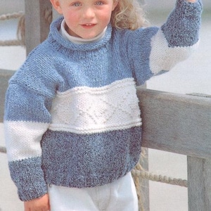 May include: A child's blue, white, and gray knit sweater with a high collar. The sweater features a color-block design with a white diamond pattern across the chest. The sleeves and lower portion of the sweater are blue.