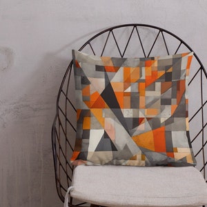 May include: A geometric patterned throw pillow with orange, gray, and white colors. The pillow is sitting on a black metal chair with a white cushion.
