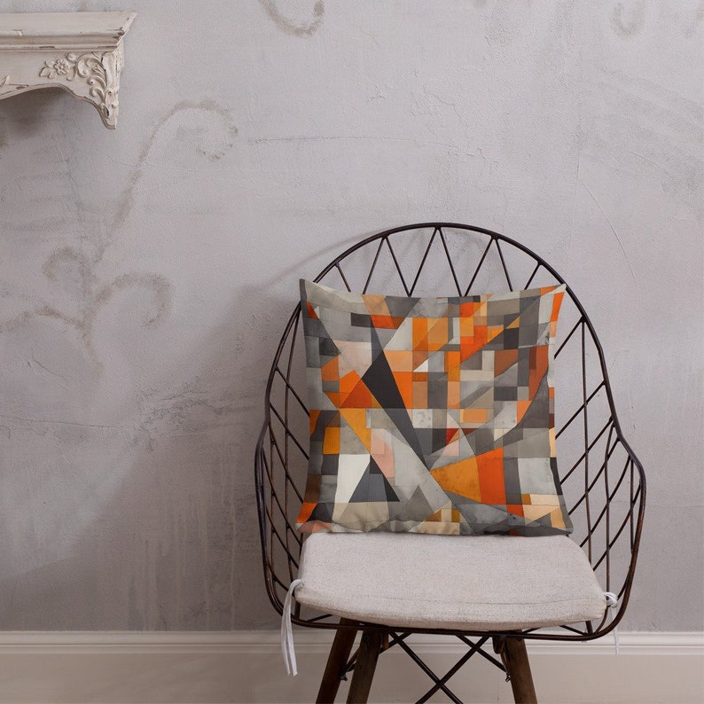 May include: A geometric patterned throw pillow with orange, gray, and white colors. The pillow is sitting on a black metal chair with a white cushion.
