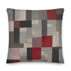 Op de afbeelding: Een decoratief kussen met een geometrisch patroon in grijstinten, rood en zwart. Het kussen heeft een modern abstract ontwerp met rechthoekige vormen.