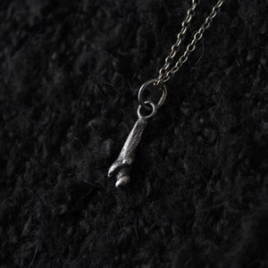 May include: A silver necklace with a small, detailed pendant shaped like a bone.