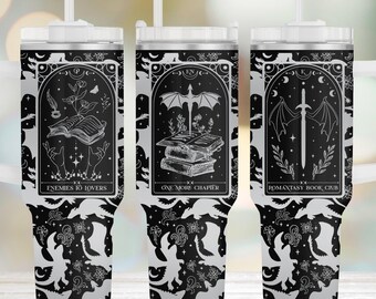 Può includere: Tre bicchieri neri e bianchi con cannuccia, ognuno caratterizzato da un design rettangolare in stile tarocchi. I disegni includono un libro aperto con fiori, un drago sopra libri impilati e una spada con ali, etichettati Enemies to Lovers, One More Chapter e Romantasy Book Club.