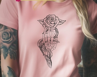 May include: A light pink t-shirt featuring a black line art graphic of a skeletal hand holding a rose with thorny stems and a spiderweb pattern. A banner at the top reads 6 FREE DESIGNS INCLUDED, and a bottom label reads KEEPSAKE HAVEN PNG | SVG.