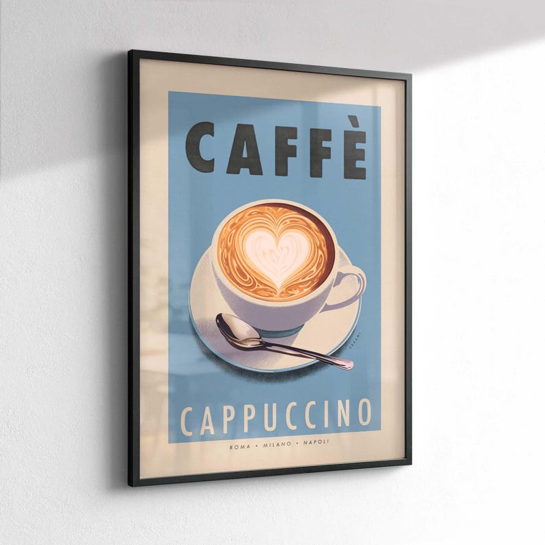 Op de afbeelding: Ingelijste kunstprint met een cappuccino met hartvormige latte art. De poster heeft een lichtblauwe achtergrond met het woord "CAFF&Egrave;" bovenaan en "CAPPUCCINO" onderaan. Een witte kop en schotel met een lepel staan in het midden.