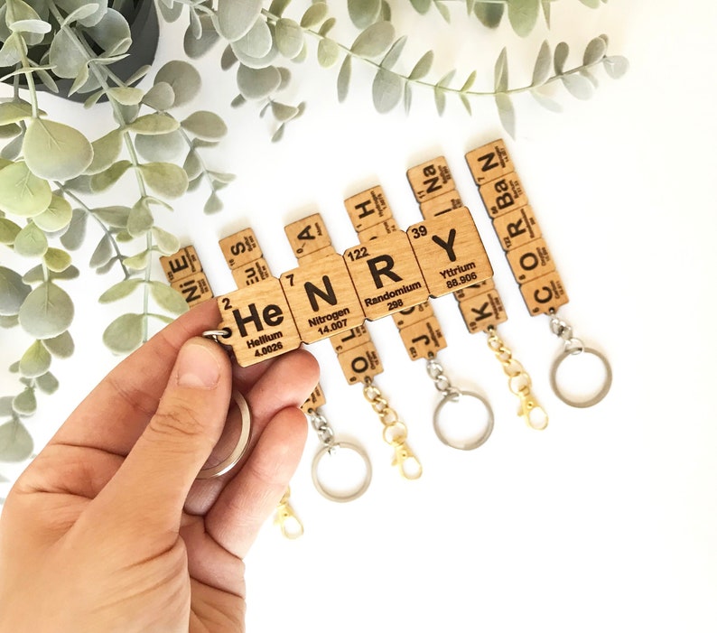 May include: Wooden keychain with the letters "HENRY" spelled out using the chemical element symbols for Helium, Nitrogen, Randomium, and Yttrium. The keychain is made of natural wood and has a gold and silver chain.