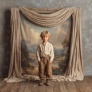 Puede incluir: Un niño pequeño está de pie frente a una pintura de paisaje, vistiendo una camisa crema con botones y pantalones marrones. El telón de fondo incluye una tela drapeada y un marco de madera. El niño tiene el pelo rubio y lleva zapatos marrones.