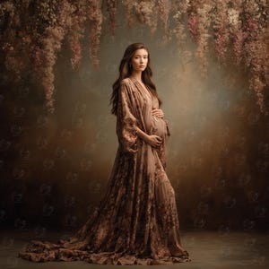 May include: A woman in a flowing, floral-print maternity gown. The dress is a muted brown with darker floral patterns. The woman is standing in front of a backdrop with hanging floral arrangements in shades of brown and pink.