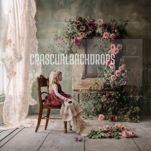 Puede incluir: Una niña con un vestido burdeos se sienta en una silla de madera frente a un telón de fondo con un espejo vintage y un arreglo floral con rosas rosas y rojas. El fondo es de color verde y marrón desgastado.