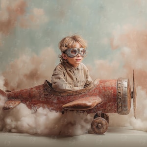 Puede incluir: Un niño con gafas de aviador y una camisa beige está sentado en un avión de juguete rojo vintage. El avión de juguete tiene una hélice y ruedas, sobre un fondo de nubes esponjosas.