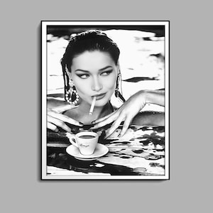 Può includere: Fotografia in bianco e nero di una donna in una piscina, che tiene una sigaretta in bocca e una piccola tazza di caffè in mano.