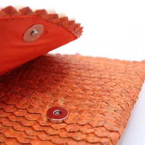 May include: Close-up of a woven orange leather clutch with a magnetic closure. The clutch is open, revealing the orange lining.