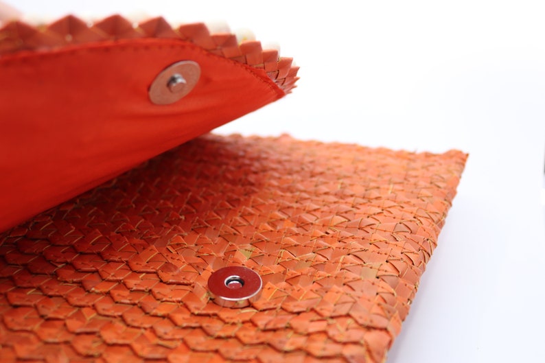 May include: Close-up of a woven orange leather clutch with a magnetic closure. The clutch is open, revealing the orange lining.
