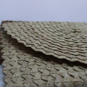 May include: Close-up of a woven, light brown, circular mat with a textured surface. The mat is made of natural materials and has a unique, intricate pattern.