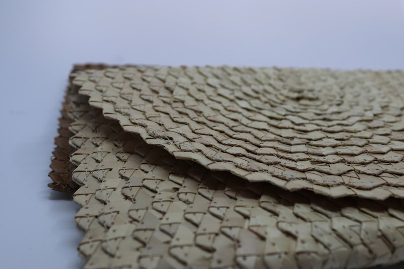 May include: Close-up of a woven, light brown, circular mat with a textured surface. The mat is made of natural materials and has a unique, intricate pattern.