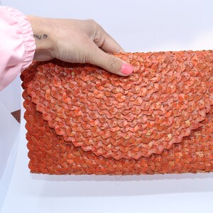 May include: A woven orange clutch bag with a unique, textured design.