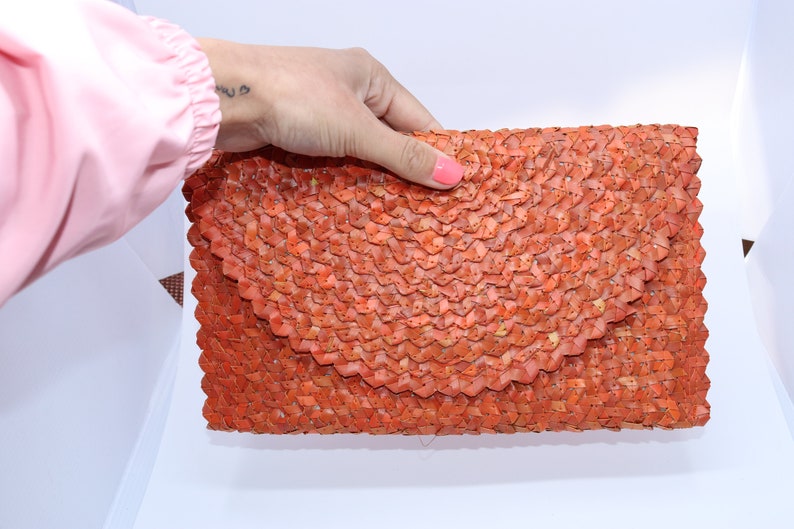 May include: A woven orange clutch bag with a unique, textured design.