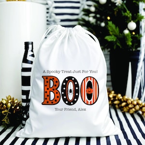 May include: White drawstring bag with the word "BOO" in orange and black, with a spider and pumpkin design. Text on the bag reads "A Spooky Treat Just For You!" and "Your Friend, Alex". A black and white striped bottle is to the left.