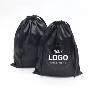 Puede incluir: Dos bolsas de cordón de satén negro. Una bolsa tiene el texto "YOUR LOGO - GOES HERE -" impreso en blanco sobre un círculo.