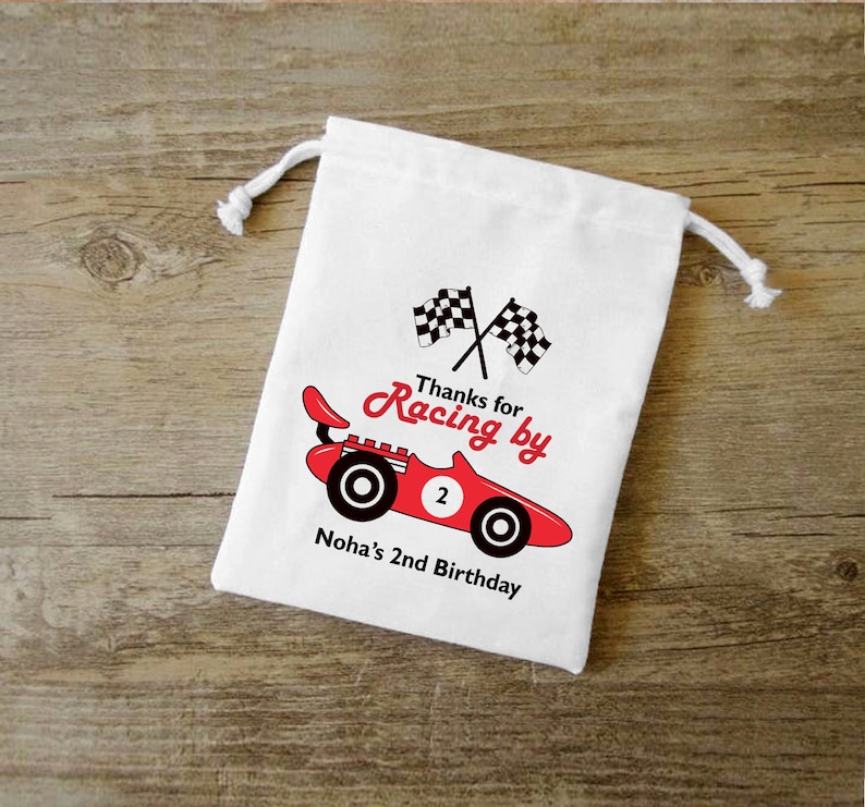 May include: White cotton drawstring bag with a red race car and checkered flags. The text on the bag reads "Thanks for Racing by Noha's 2nd Birthday."