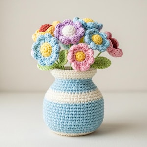 May include: A handmade crochet bouquet of colorful flowers in a blue and white striped vase. The flowers are in shades of blue, pink, yellow, purple, and red, with green leaves. The vase is approximately 6 inches tall.