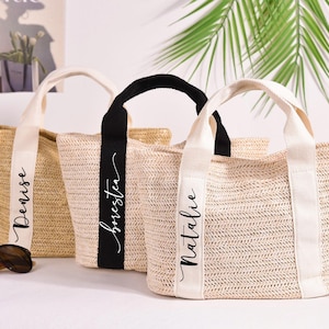 Könnte beinhalten: Drei Strohtaschen mit schwarzen und weißen Stoffbändern. Die Taschen sind mit den Namen "Denise", "Brester" und "Natalie" in weißer Schrift personalisiert.