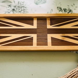 Puede incluir: Una bandeja rectangular de madera con un diseño de Union Jack. La bandeja está hecha de madera marrón claro con una incrustación de madera marrón oscuro para el diseño de la bandera.