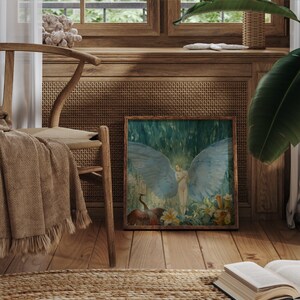 May include: A framed artwork depicts a nude figure with large blue wings, set against a backdrop of lush greenery and flowers. The artwork is displayed on a wooden floor, next to a woven chair with a blanket draped over it, creating a serene, artistic ambiance.