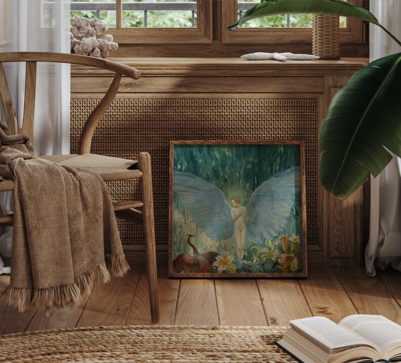 May include: A framed artwork depicts a nude figure with large blue wings, set against a backdrop of lush greenery and flowers. The artwork is displayed on a wooden floor, next to a woven chair with a blanket draped over it, creating a serene, artistic ambiance.