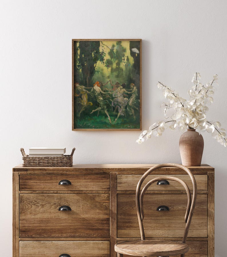 May include: A framed artwork depicts figures dancing in a forest setting. The painting features a palette of greens, yellows, and browns, with a focus on movement and light. The artwork is displayed above a wooden dresser with a woven basket and a vase of white flowers.
