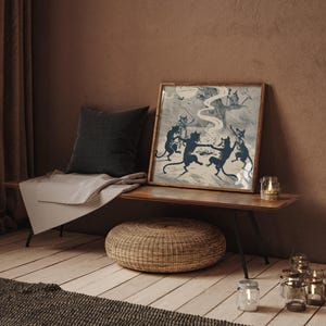 May include: A framed print depicts dancing black cats around a bonfire, with a full moon in the background. The print is displayed on a wooden bench with a dark gray pillow and a striped blanket. A woven ottoman and candles complete the scene.