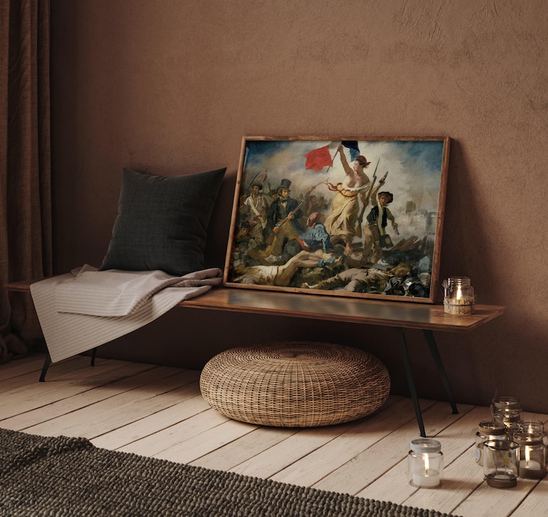 May include: A framed print of a classic painting depicting a historical scene with figures and a flag. The artwork is displayed on a wooden bench with a dark gray pillow and a light gray blanket. A woven ottoman and candles are in the foreground.