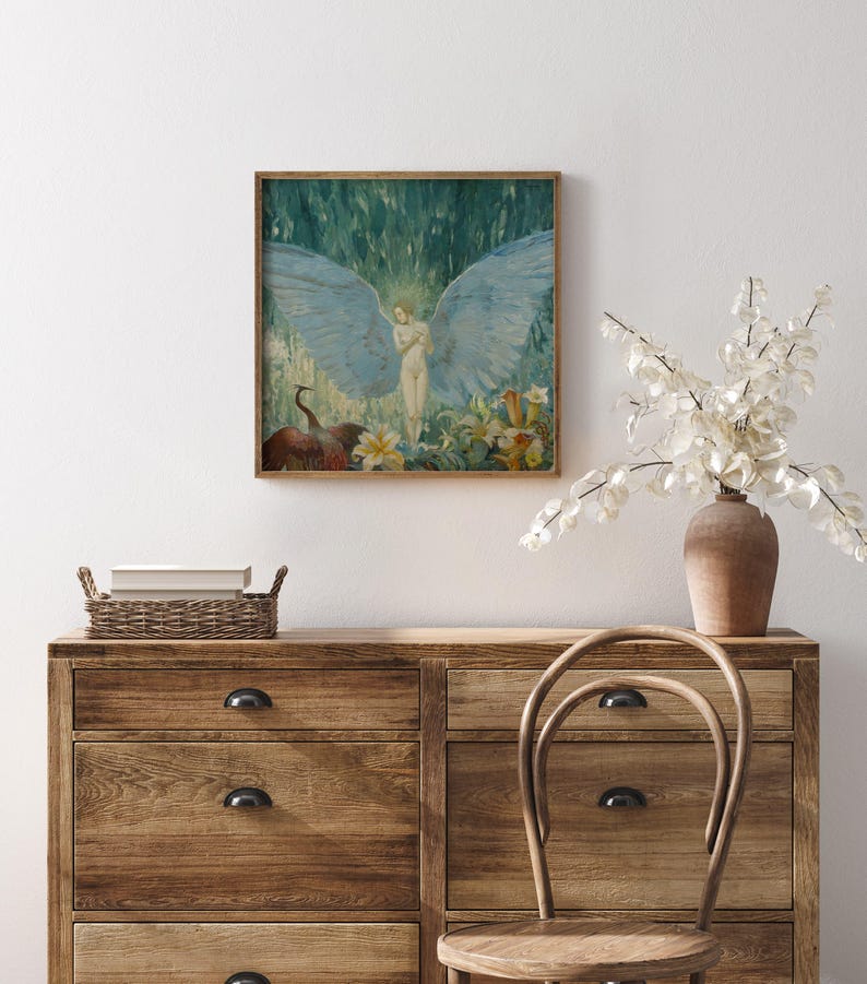 May include: A framed artwork depicts a nude figure with large blue wings, surrounded by flowers and a bird. The painting has a vintage aesthetic with a wooden frame. The artwork is displayed above a wooden dresser with a woven basket and a vase of white flowers.