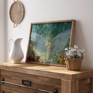 May include: A framed artwork featuring a nude figure with large blue wings, set against a backdrop of lush greenery. The artwork is displayed on a wooden dresser, alongside a white pitcher and a small basket of white flowers.