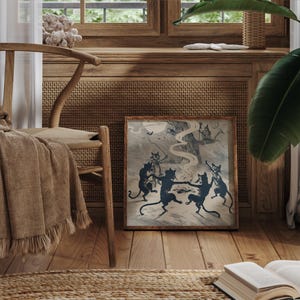 May include: A framed vintage print depicts silhouetted cats dancing in a circle under a full moon. The artwork, in shades of blue and gray, is set against a backdrop of a spooky tree and a distant house. The print is displayed on a wooden floor.