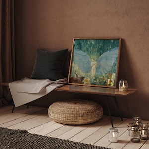 May include: A framed artwork depicting a nude figure with large blue wings, set against a backdrop of green foliage. The artwork is displayed on a wooden bench with a dark gray pillow, a striped blanket, and a woven ottoman. Several glass candle holders are also present.
