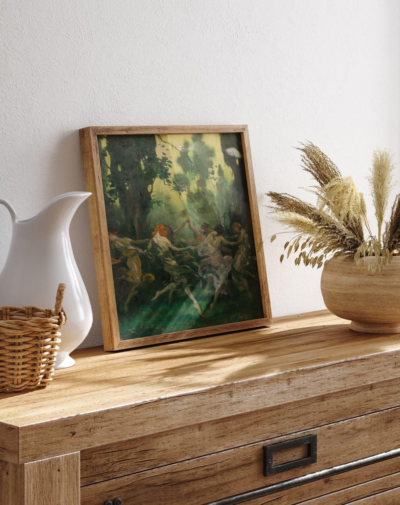 May include: A framed vintage painting with a wooden frame depicts figures dancing in a forest setting. The artwork features a palette of greens, yellows, and browns. The painting rests on a wooden dresser, next to a white pitcher and a woven basket.