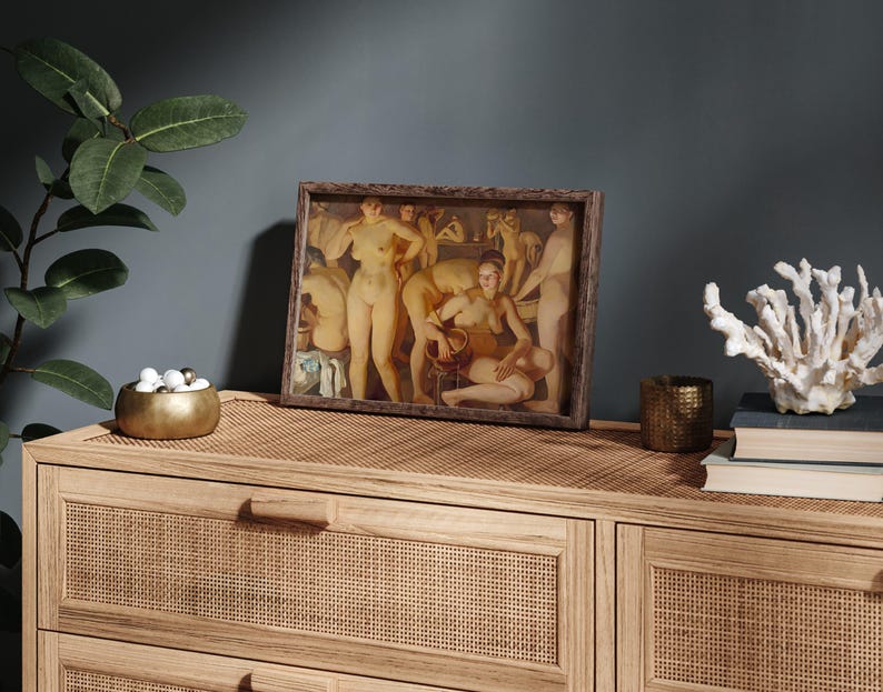 May include: A framed artwork depicting a classical scene with nude figures in warm tones. The artwork is displayed on a light wood dresser with a woven top, alongside decorative items like a gold bowl, candle holder, and coral.