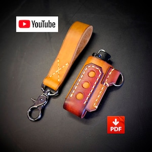 May include: A brown leather lighter case with a tan leather strap and a metal clip. The case has a red stitching detail and three holes for a lighter. The strap has a white X stitched into it. The case is for a lighter and has a PDF download icon.
