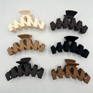 Peut inclure: Six pinces à cheveux en plastique de différentes couleurs : beige, marron, noir, marron foncé et marron clair. Les pinces sont toutes du même design, avec une forme incurvée et plusieurs dents.
