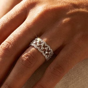 May include: A silver ring featuring a repeating geometric pattern of small triangles, set with sparkling gemstones. The ring is worn on a finger, with the brand name "Alignment Heart" visible below.