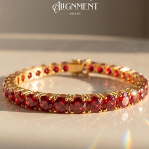 May include: A gold bracelet with a series of red gemstones. The bracelet is set with multiple round-cut, red gemstones. The clasp is gold. The text "Alignment Heart" is in the upper left corner.