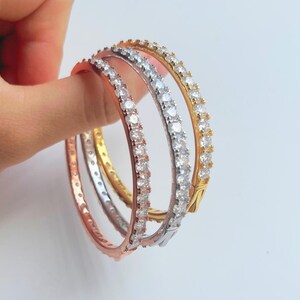 Op de afbeelding: Drie armbanden in goud, zilver en roségoud, elk met een rij heldere zirkonia-stenen.