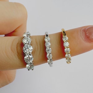 Pode incluir: Três anéis de prata e ouro com pedras redondas e transparentes. Os anéis estão em um dedo.