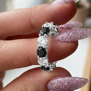 Peut inclure: Une alliance en argent ornée d'un motif alterné de pierres rondes noires et blanches transparentes serties sur griffes. La bague porte l'inscription ALIGNMENT HEART en haut. Le design présente une rangée continue de pierres serties.