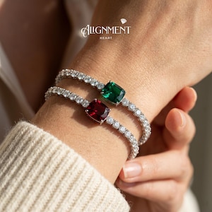 May include: Two silver bracelets with clear and sparkling stones. Each bracelet features a large, square-cut gemstone, one red and one green. The bracelets are worn on a wrist, with the brand name "Alignment Heart" visible.