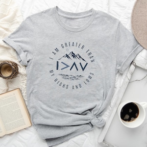 May include: Gray t-shirt with a graphic design of mountains and a symbol that reads "I am greater than my highs and lows".